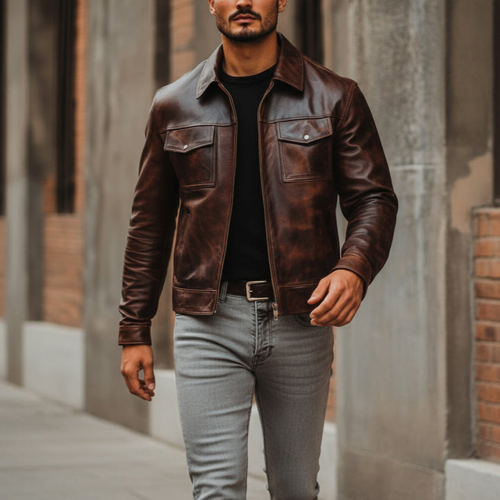 Man wearing a brown leather jacket and gray jeans standing in an urban setting.
